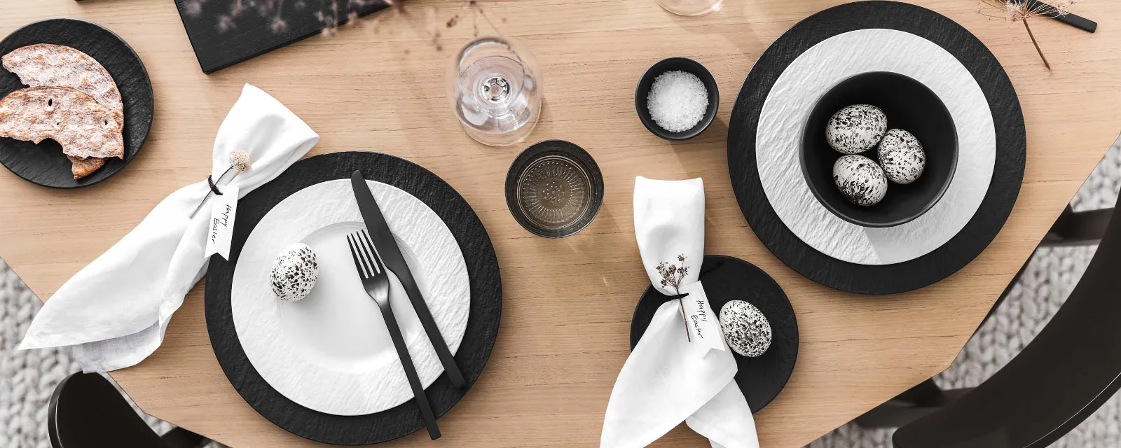 A modern dining table with black and white crockery and cutlery from the Manufacture collection and minimalist Easter decorations.