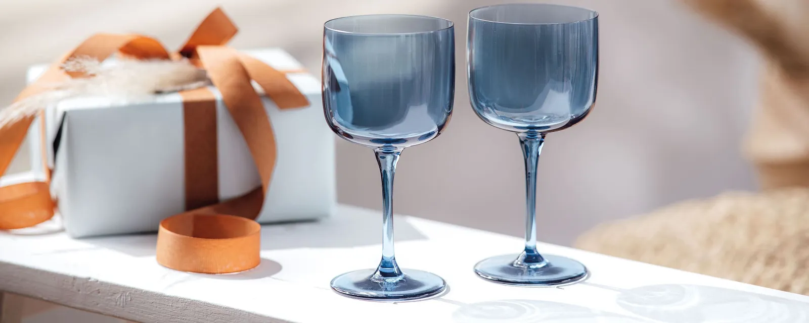 Two blue like. wine glasses on a table next to a gift box.