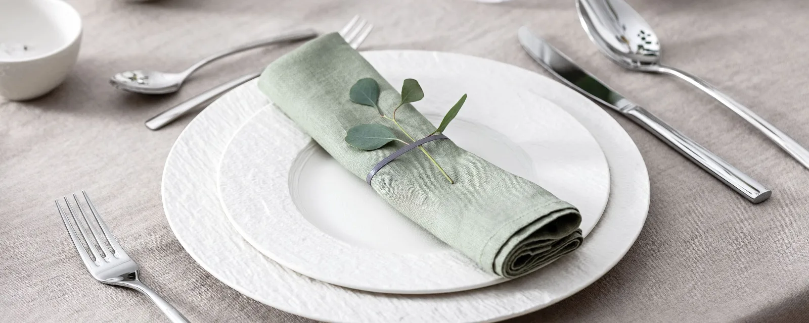 A table set with two white Manufacture plates, a pastel-green napkin, Piedmont cutlery and eucalyptus.