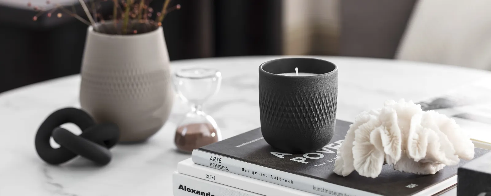 Elegant home decor arrangement with a black Manufacture scented candle, books and a light-grey Manufacture vase on a marble table.