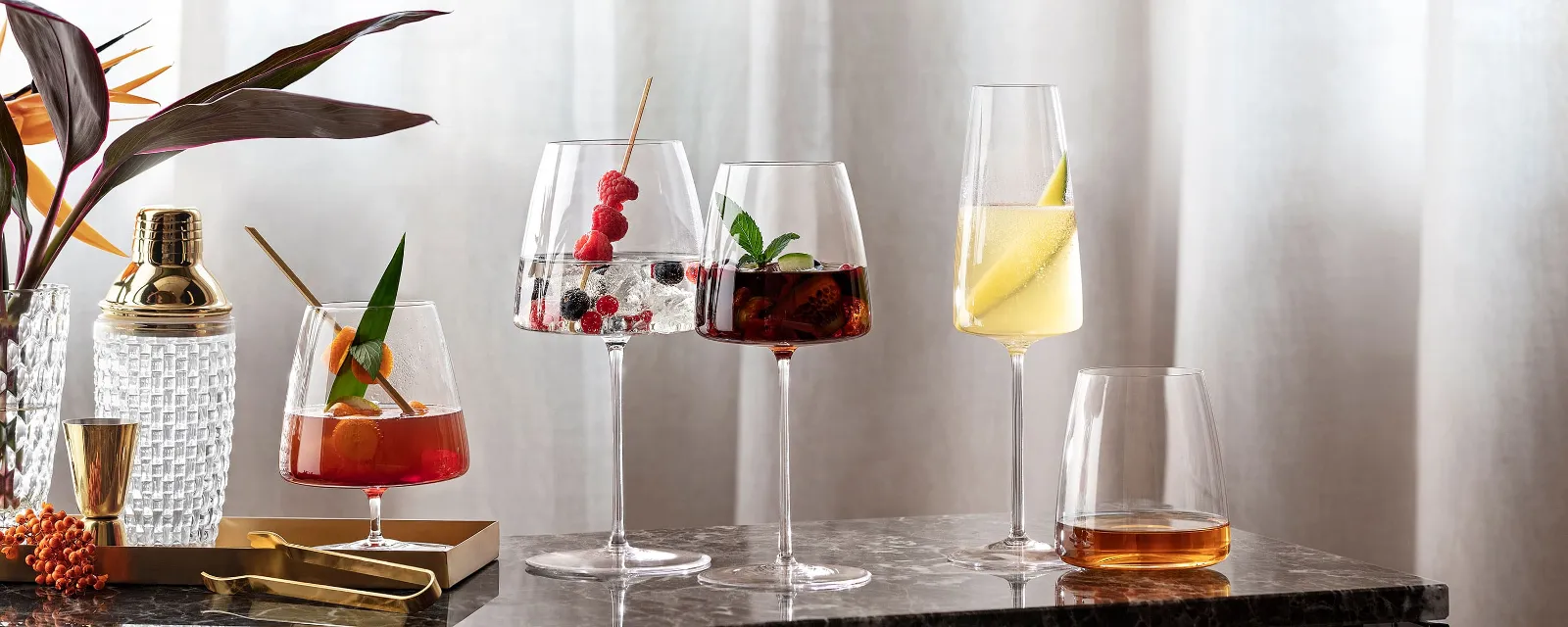 Various cocktails in elegant MetroChic glasses on a marble table next to a plant.