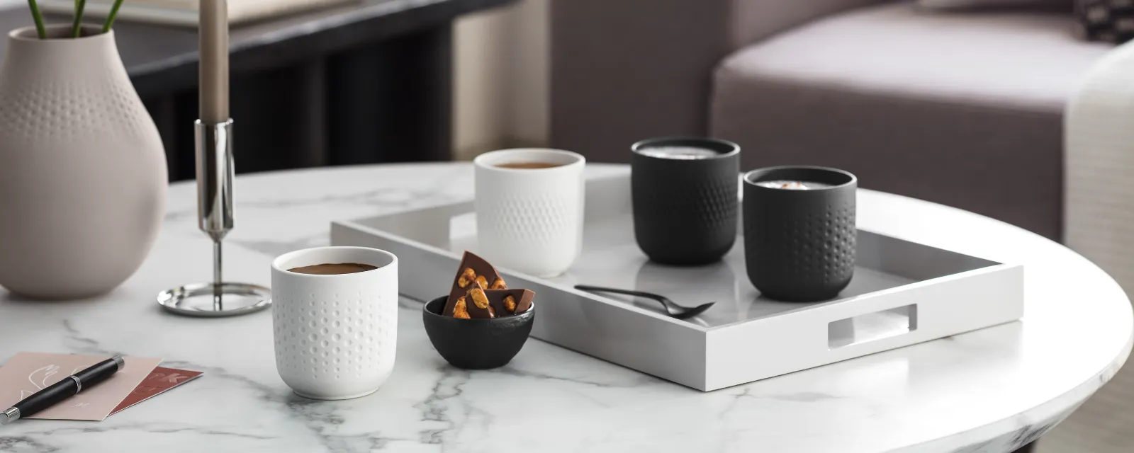 Elegant coffee table in a living room with Manufacture coffee mugs, candles, vases and a tray with cups and snacks.