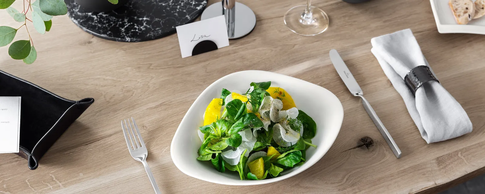 A Villeroy & Boch Vapiano bowl with salad on a wooden table, beside a NewWave knife and fork.