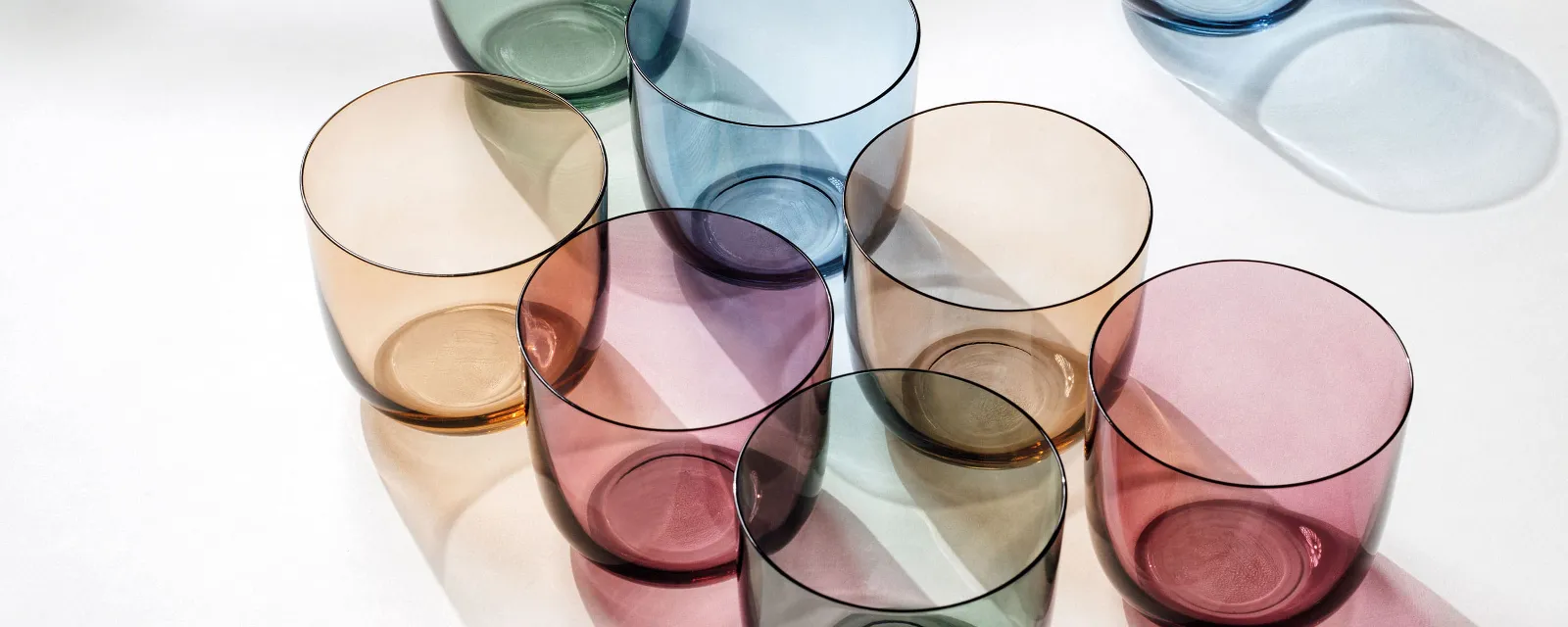 Water glasses in different colours from like. by Villeroy & Boch arranged on a white surface.