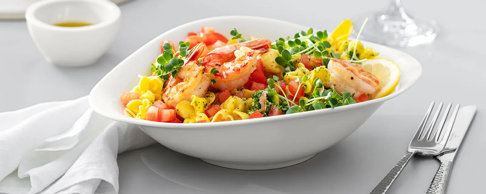 Villeroy & Boch Vapiano plate filled with a pasta salad on a wooden table. On the table there is a Villeroy & Boch wine glass and cutlery 