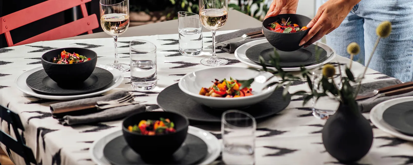 A woman setting a table with NewMoon and Manufacture plates and bowls for a barbecue evening outdoors.