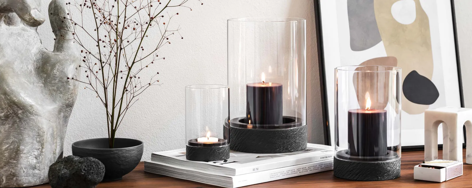 A modern home interior with a wooden sideboard and a dried flower with three Manufacture hurricane lamps.