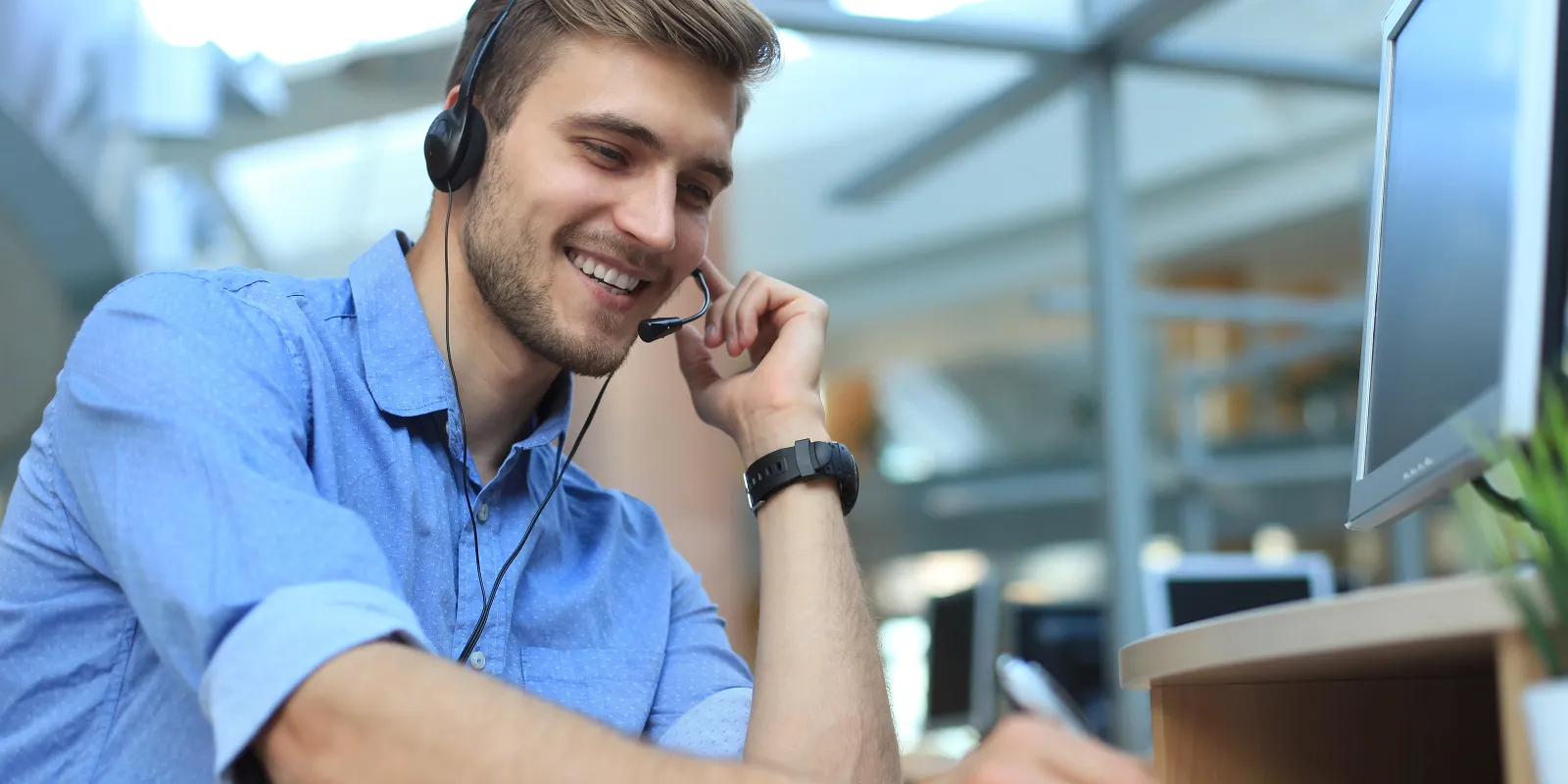 Smiling man with headset working on a computer in an office environment.