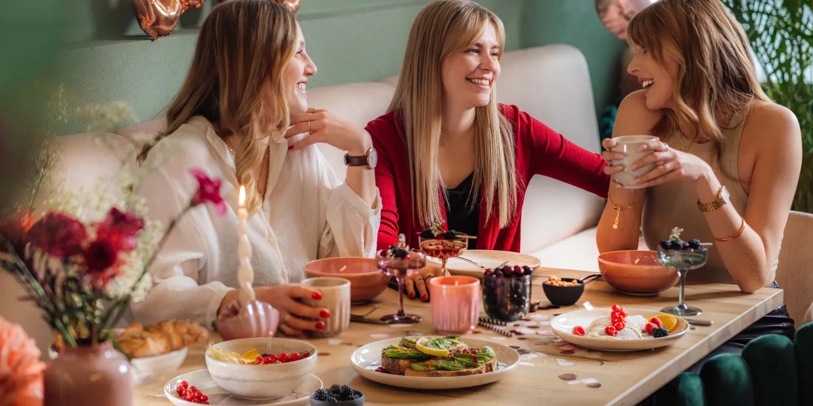 A festive scene with three women at a table with Perlemor crockery and Like Glass from like. by Villeroy & Boch, with balloons in the background.