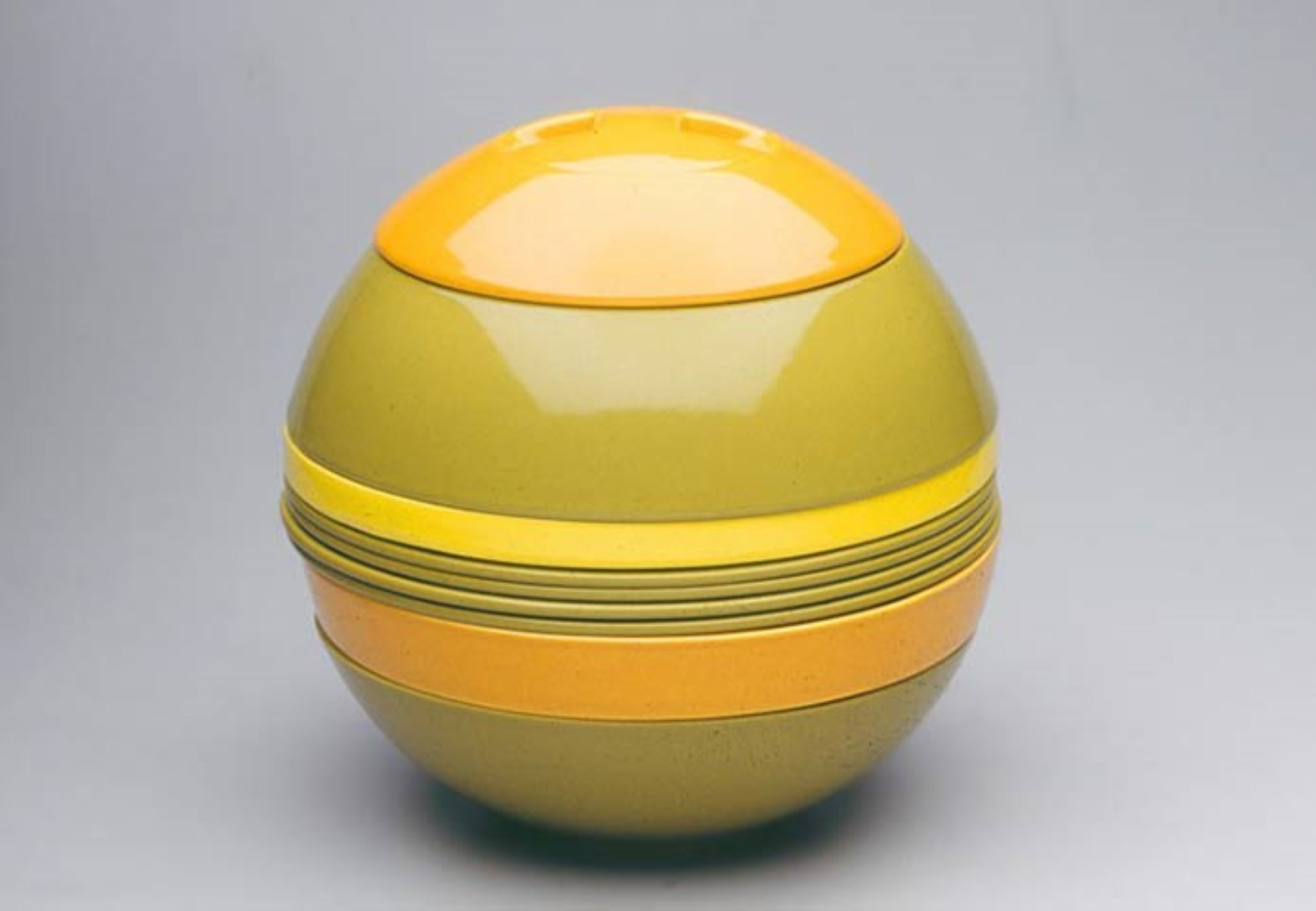 vb-laboule-history-1971 La Boule, round container with smooth surface, yellow and orange ribbons on a light gray background.