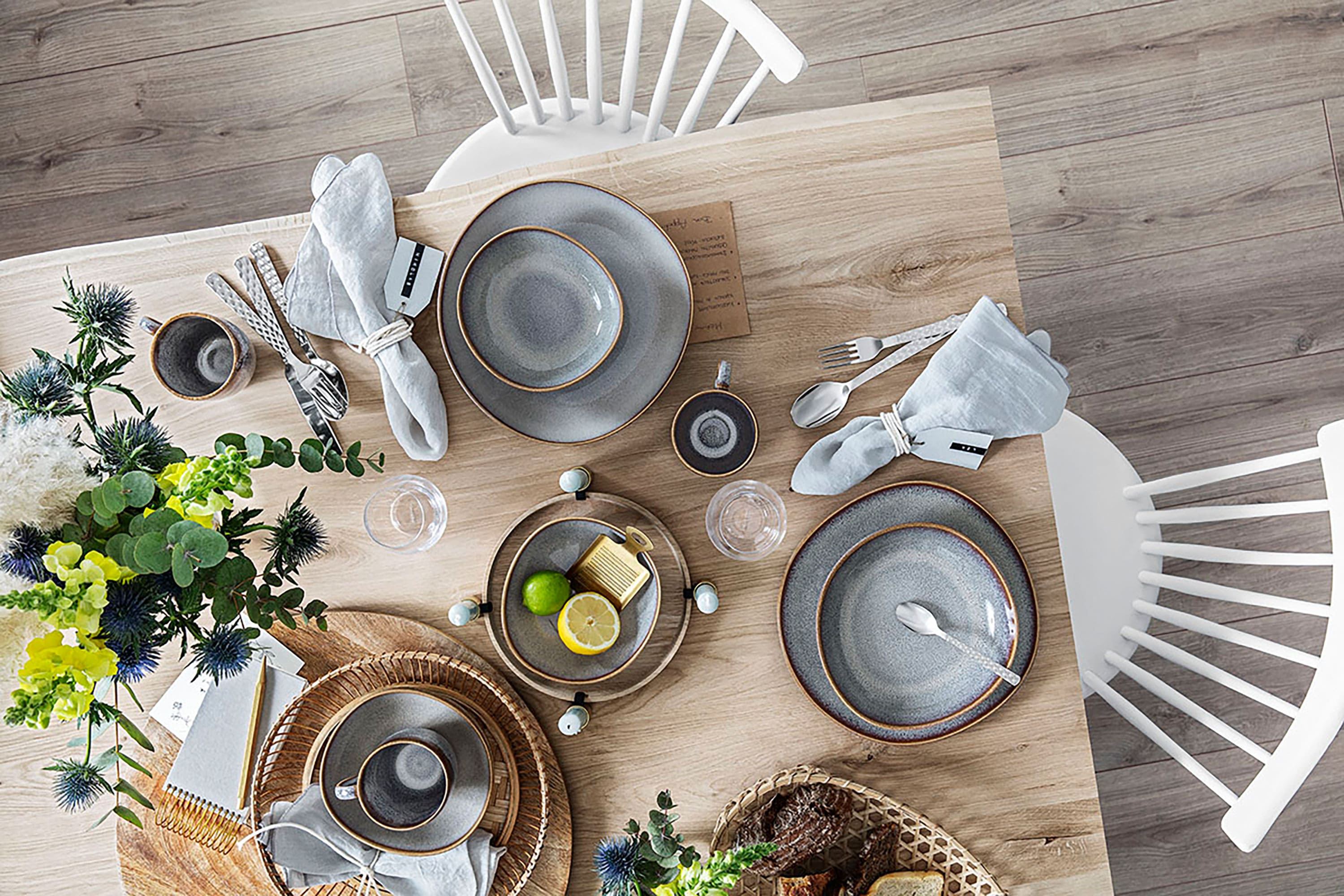 Modernen Esstisch gedeckt mit Lave Tellern, silbernem Besteck, Gläsern mit Limette und weißen Stühlen auf einem Holzboden.