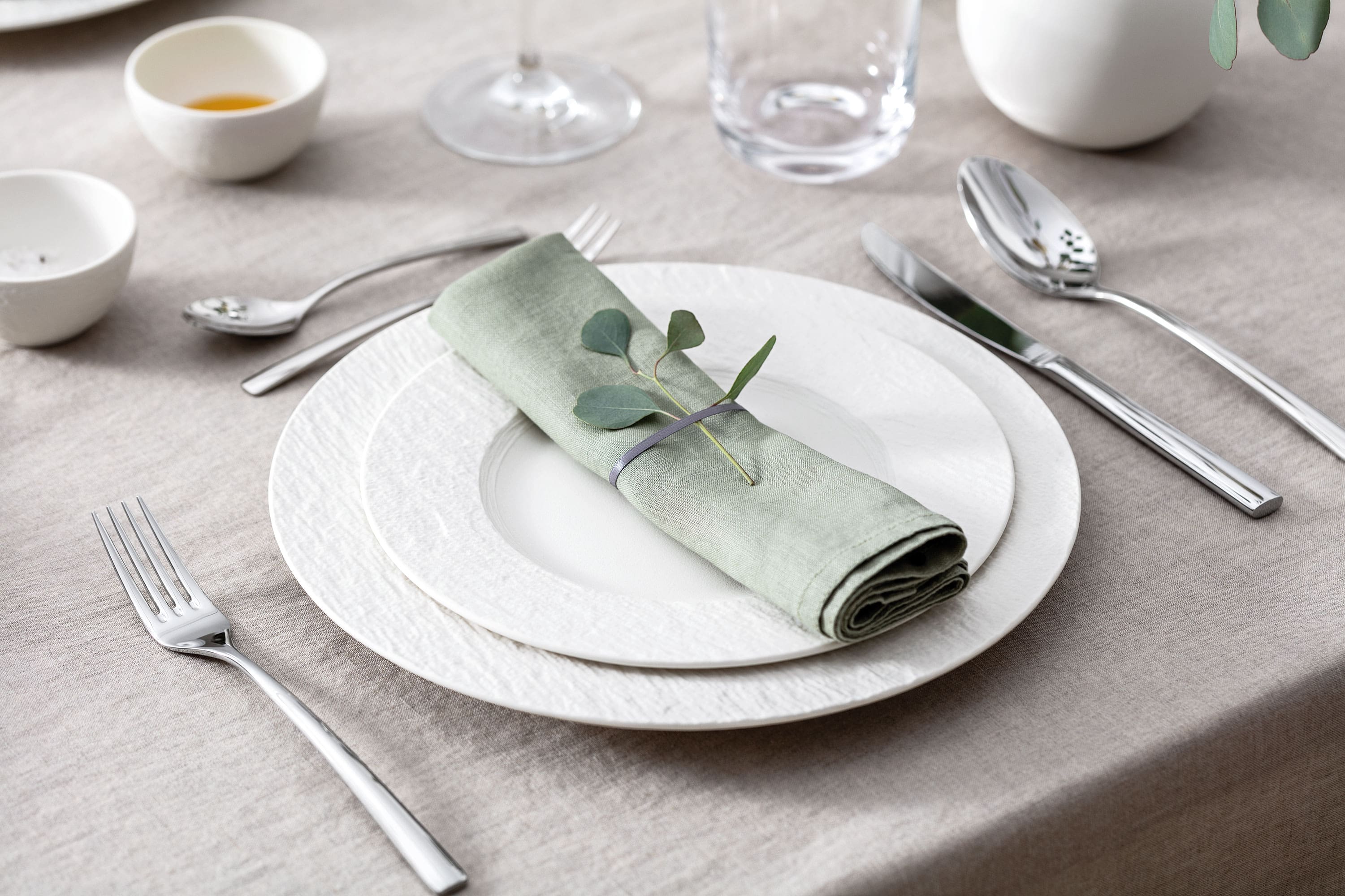 A table set with two white Manufacture plates, a pastel-green napkin, Piedmont cutlery and eucalyptus.