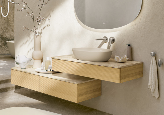 Moderner Waschtisch mit Aufsatzwaschbecken aus der Antao-Kollektion, kombiniert mit hellen Holzoberflächen, organischen Formen und natürlichem Licht in einem minimalistischen Badezimmer.