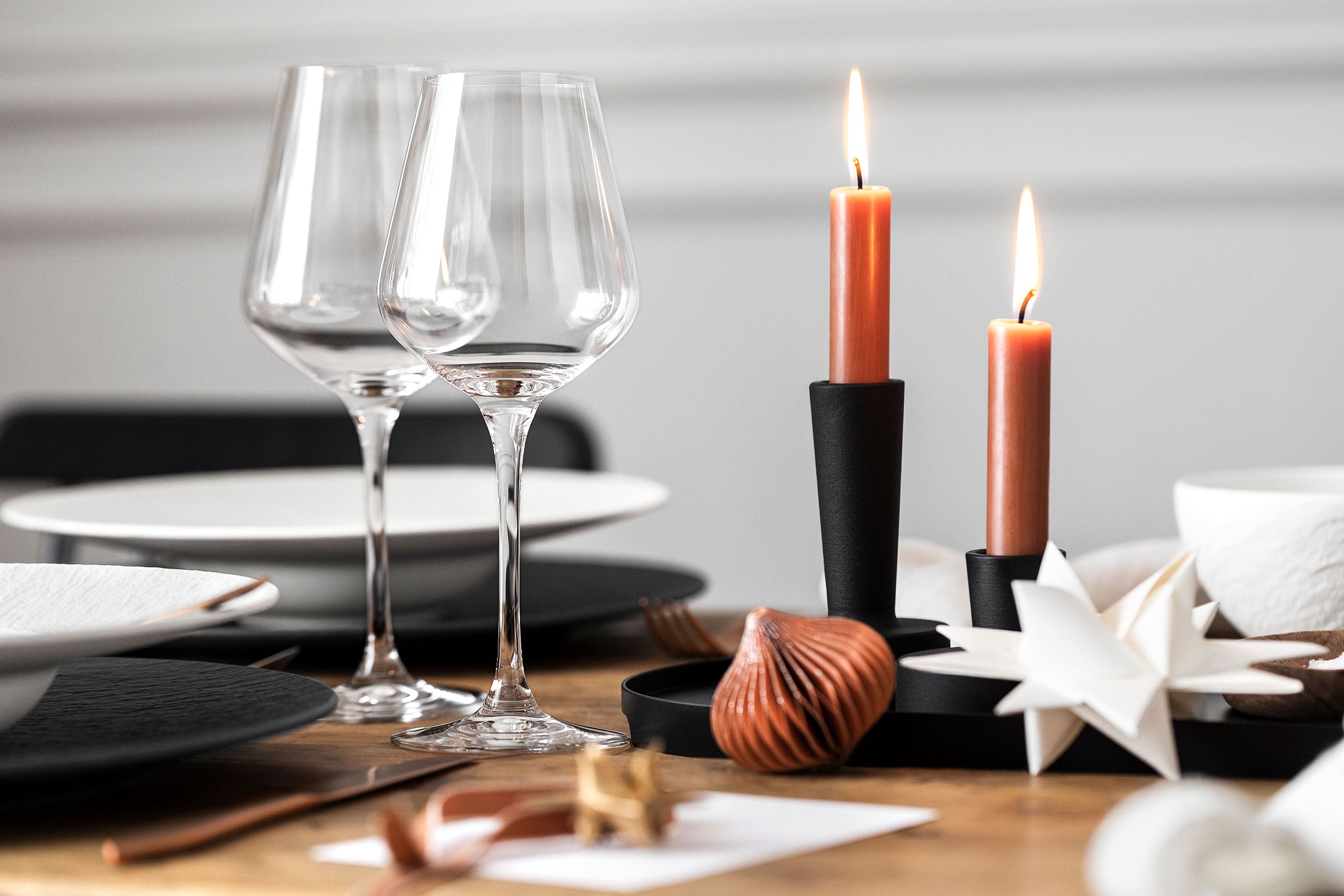 La Divina wine glasses from Villeroy & Boch with black candle holders. La Divina wine glasses from Villeroy & Boch, a black candle holder with two burning candles, all elegantly surrounded by decorative elements.