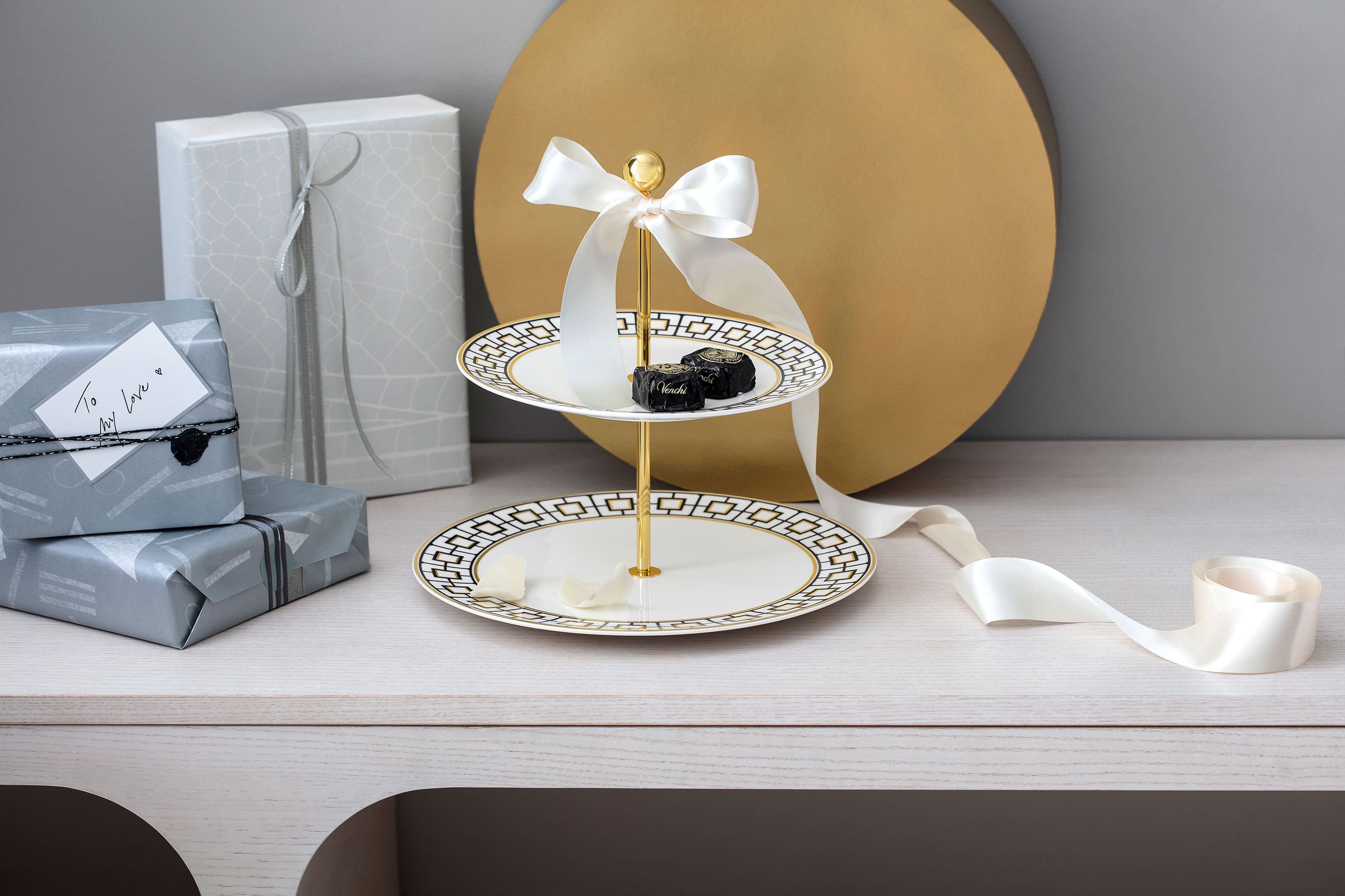  Een MetroChic etagère met gebak omringd door geschenkdozen en een strik op een houten tafel.