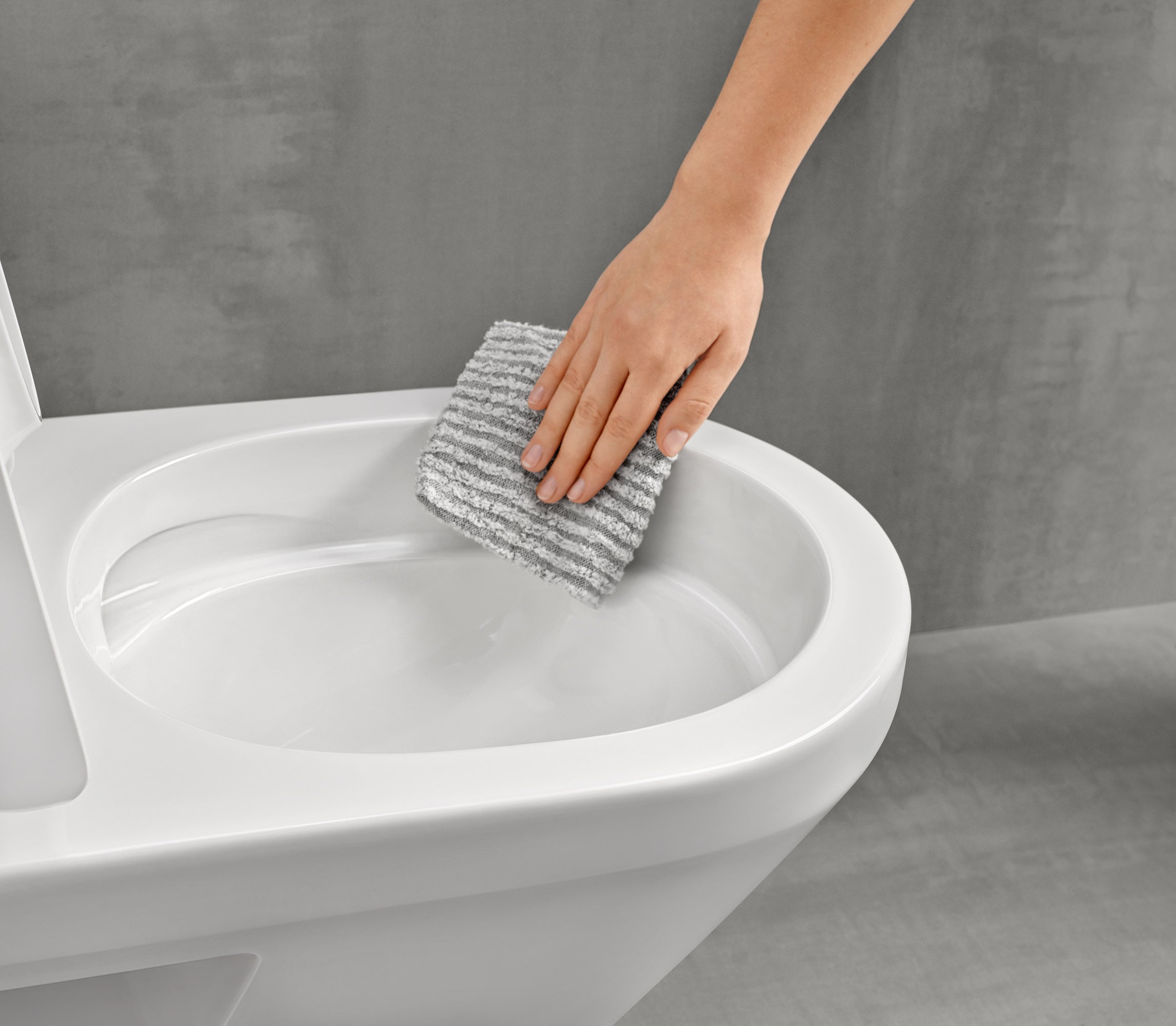 Reinigung eines Villeroy & Boch WC Eine Hand wischt mit einem weißen Tuch ein weißes Keramik-WC ab.