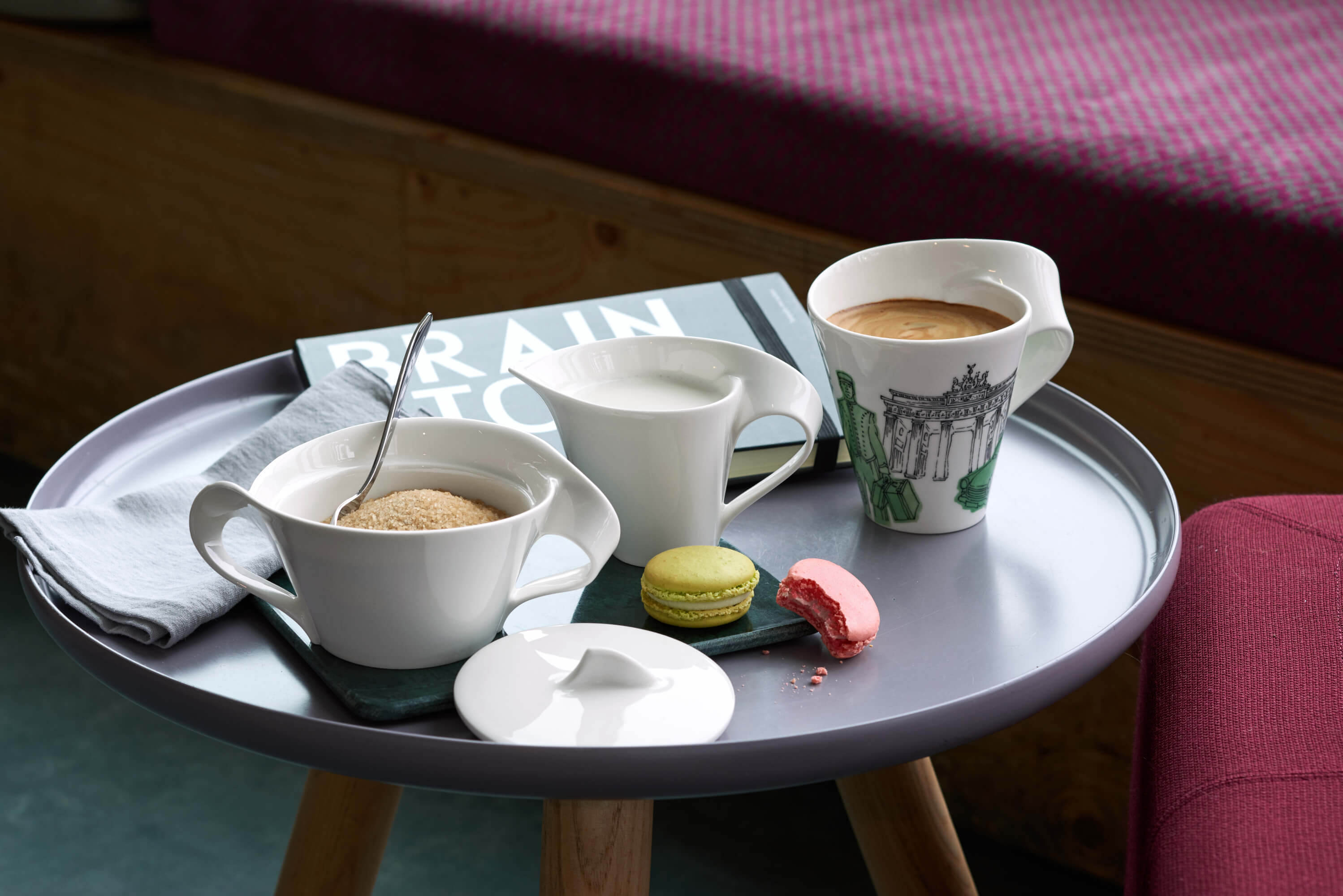 Set da caffè NewWave con macarons su un tavolino Tazza da caffè NewWave, lattiera, zuccheriera con cucchiaio e due macarons su un piattino, su un tavolino.