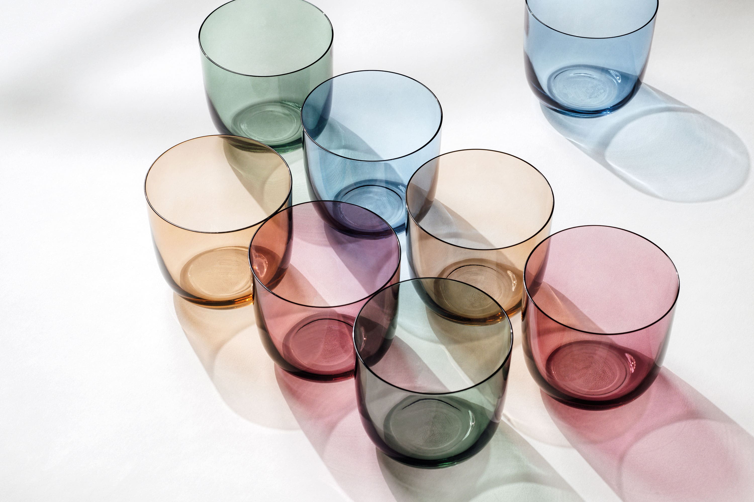 Water glasses in different colours from like. by Villeroy & Boch arranged on a white surface.