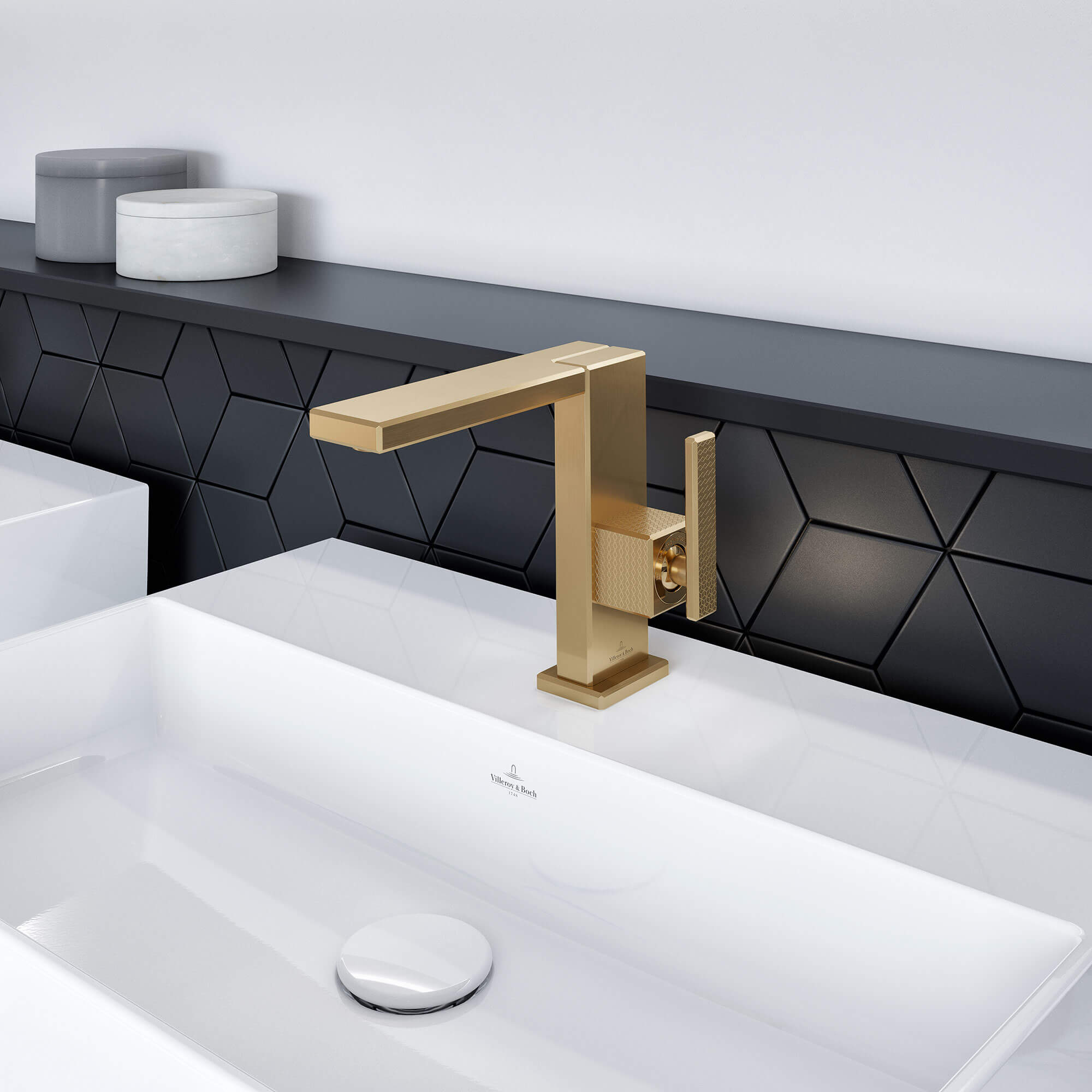 Złota bateria Mettlach na białej umywalce Nowoczesna złota bateria zamontowana na białej umywalce z czarną geometryczną ścianką w łazience.