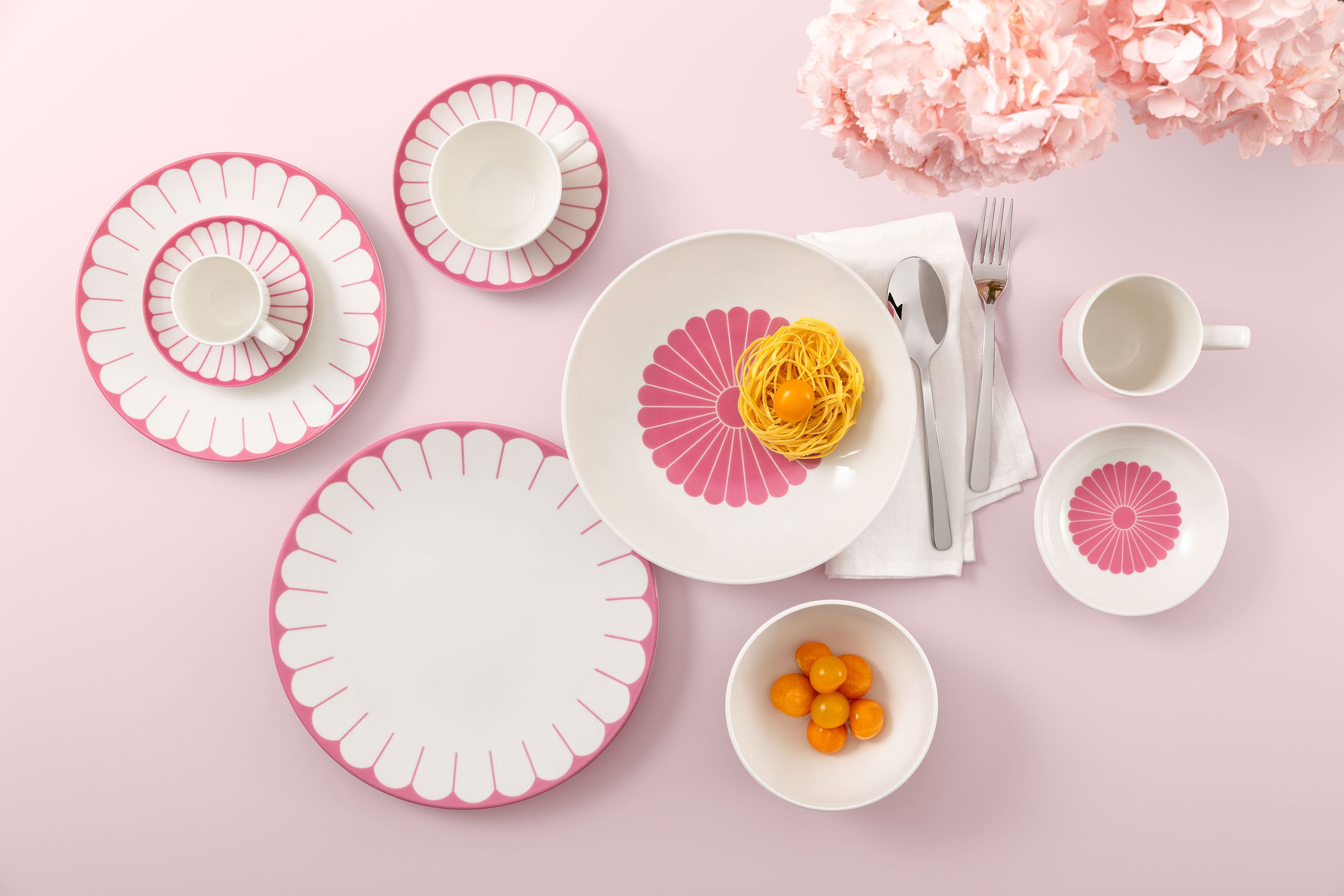 Table setting with Villeroy & Boch Fleur Cassis plates, pasta, clementines, and flowers on a pink background.