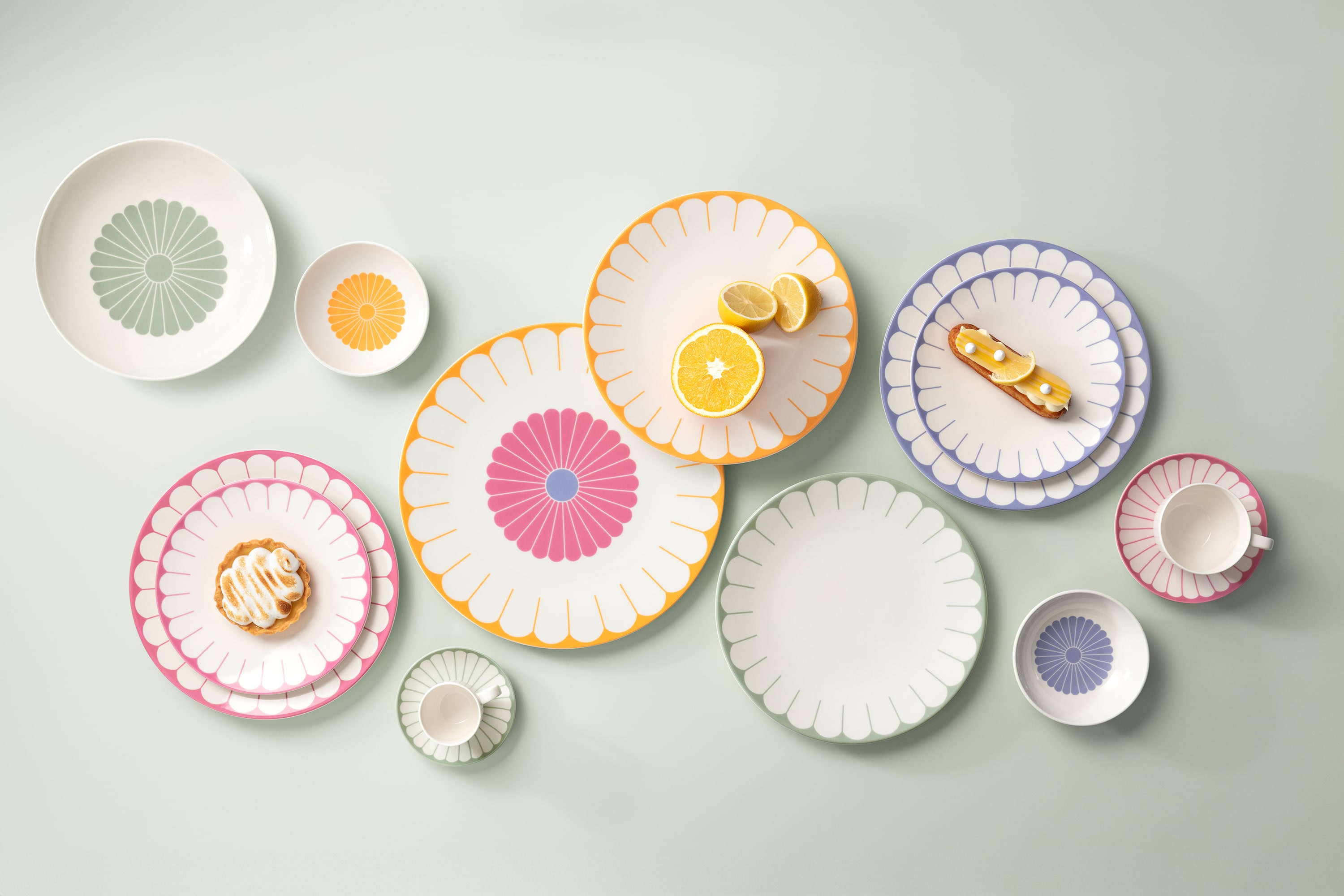 Various colourful, patterned plates, bowls and a cup are arranged on a light-coloured surface, each with a different design. Pastries are placed on some of the plates.	