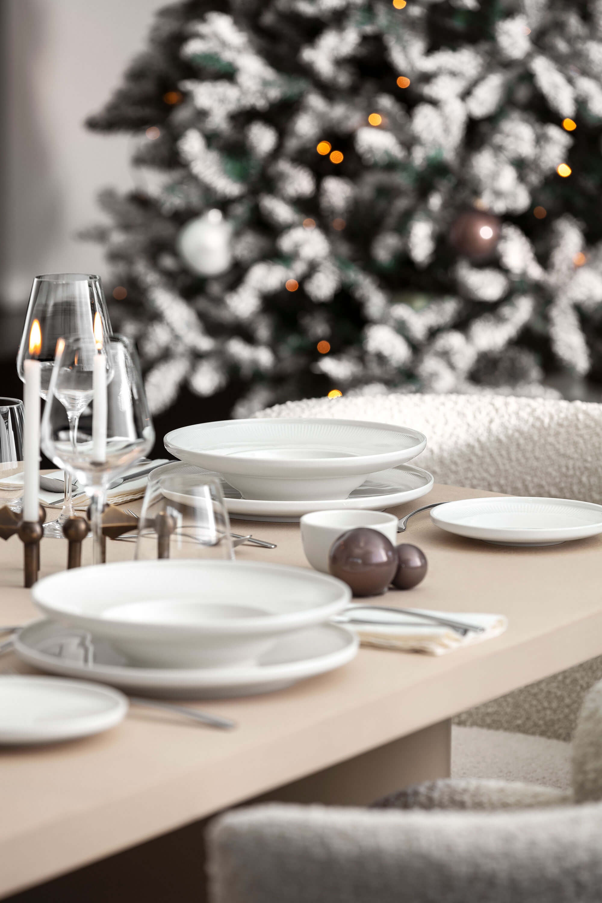Afina plates on a festively decorated table A dining table setting with white Afina plates, bowls and glasses next to a Christmas tree decorated with lights and ornaments.