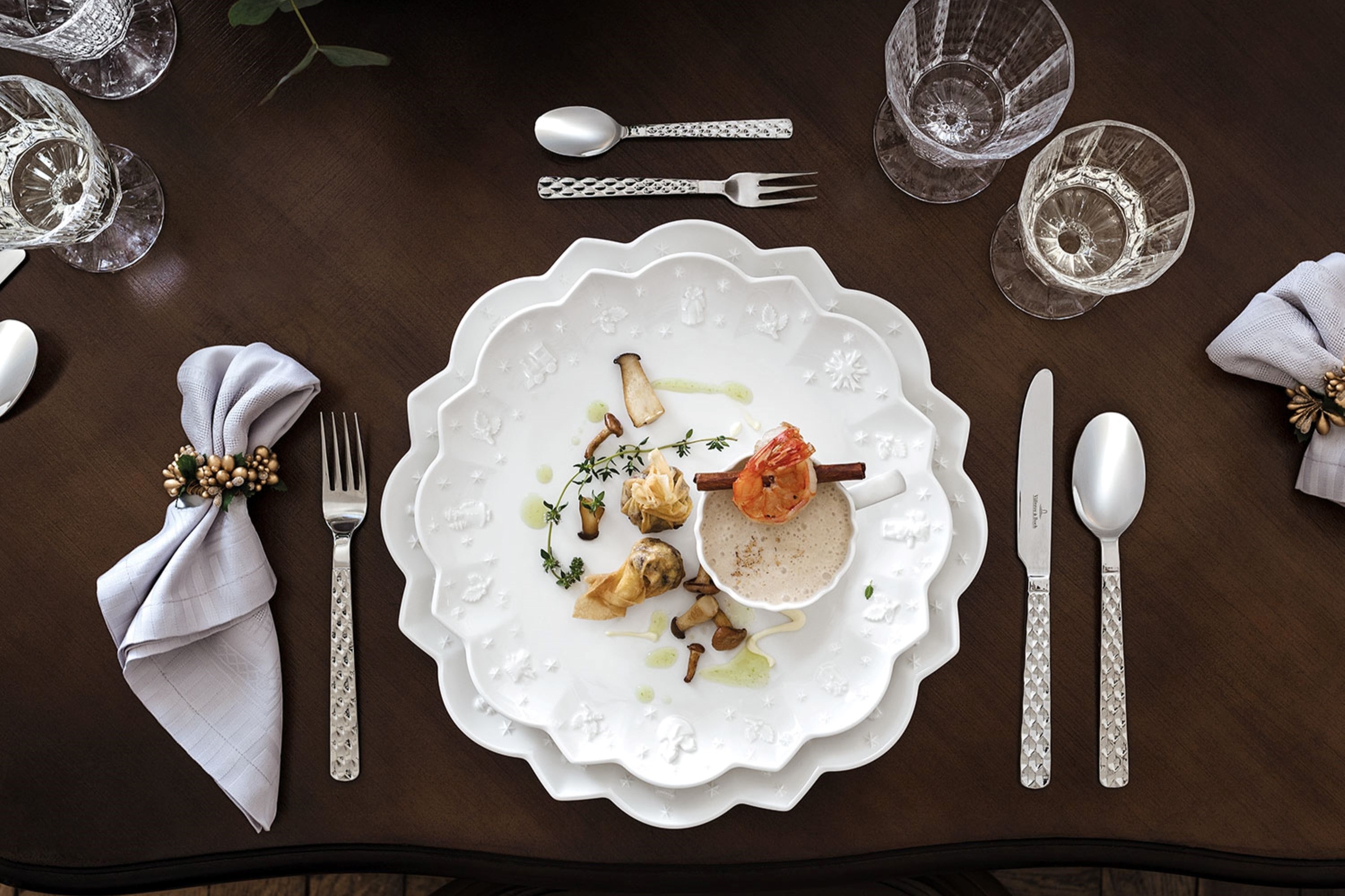 Boston flatware with Toy’s Delight Christmas dinnerware A sophisticated dining table arrangement presents the “Boston” plates from Villeroy & Boch, which are artfully decorated with a wave pattern, and garnishes them with crystal glasses, richly decorated silver flatware, and decorative napkins on a dark wooden table.