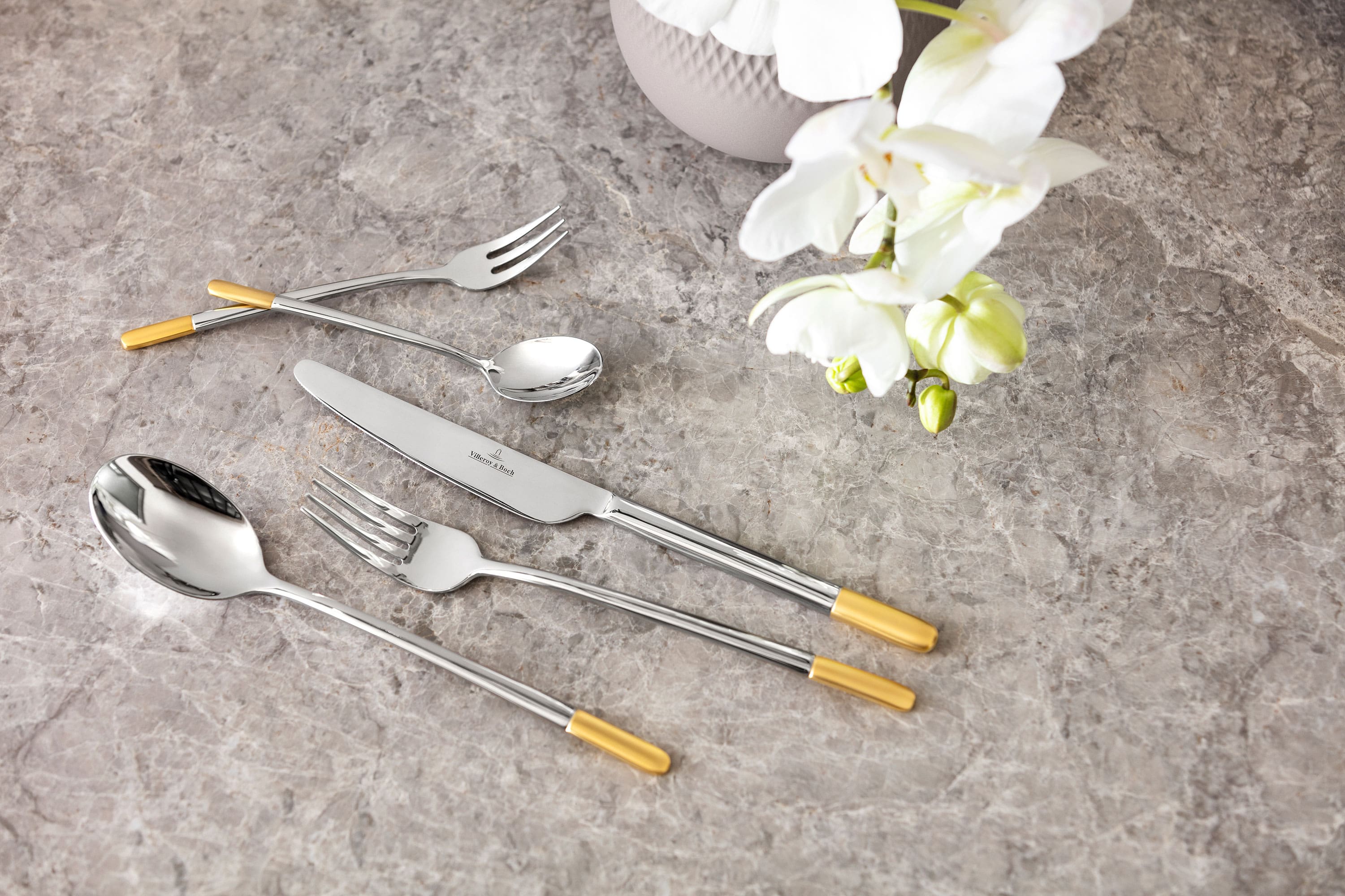 Elegant Ella cutlery set with gold details on a marble table top, together with a white orchid.