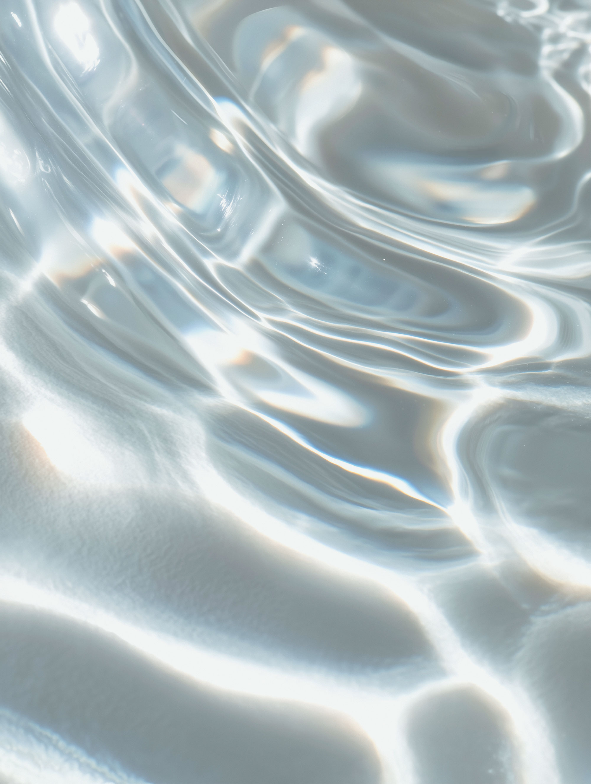 La luz del sol se refleja en las suaves olas del agua clara, creando brillantes patrones ondulados en la superficie.