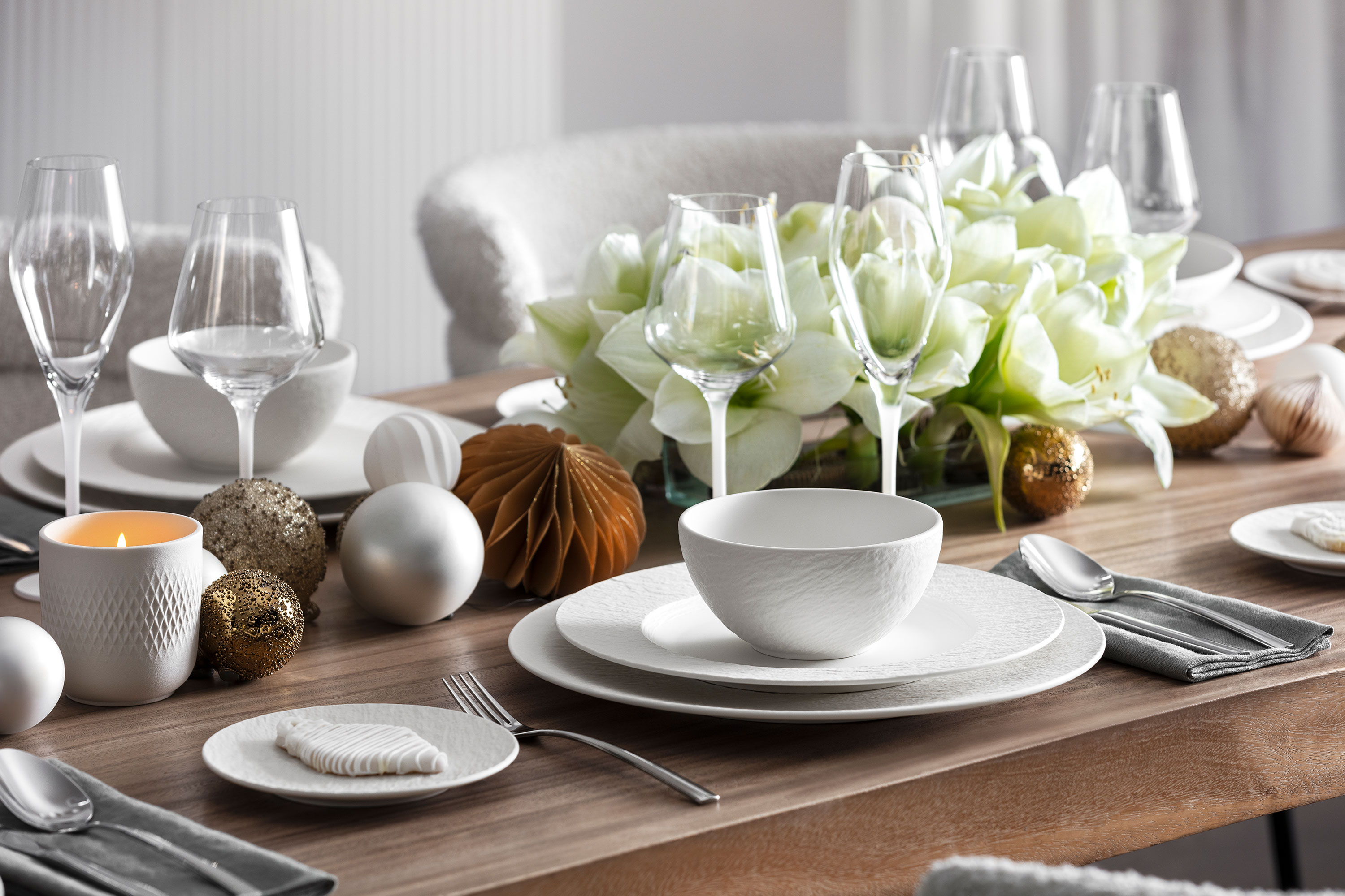 Elegant table setting with Manufacture dinnerware, glassware, silverware, and a centerpiece of white flowers and decorative ornaments.