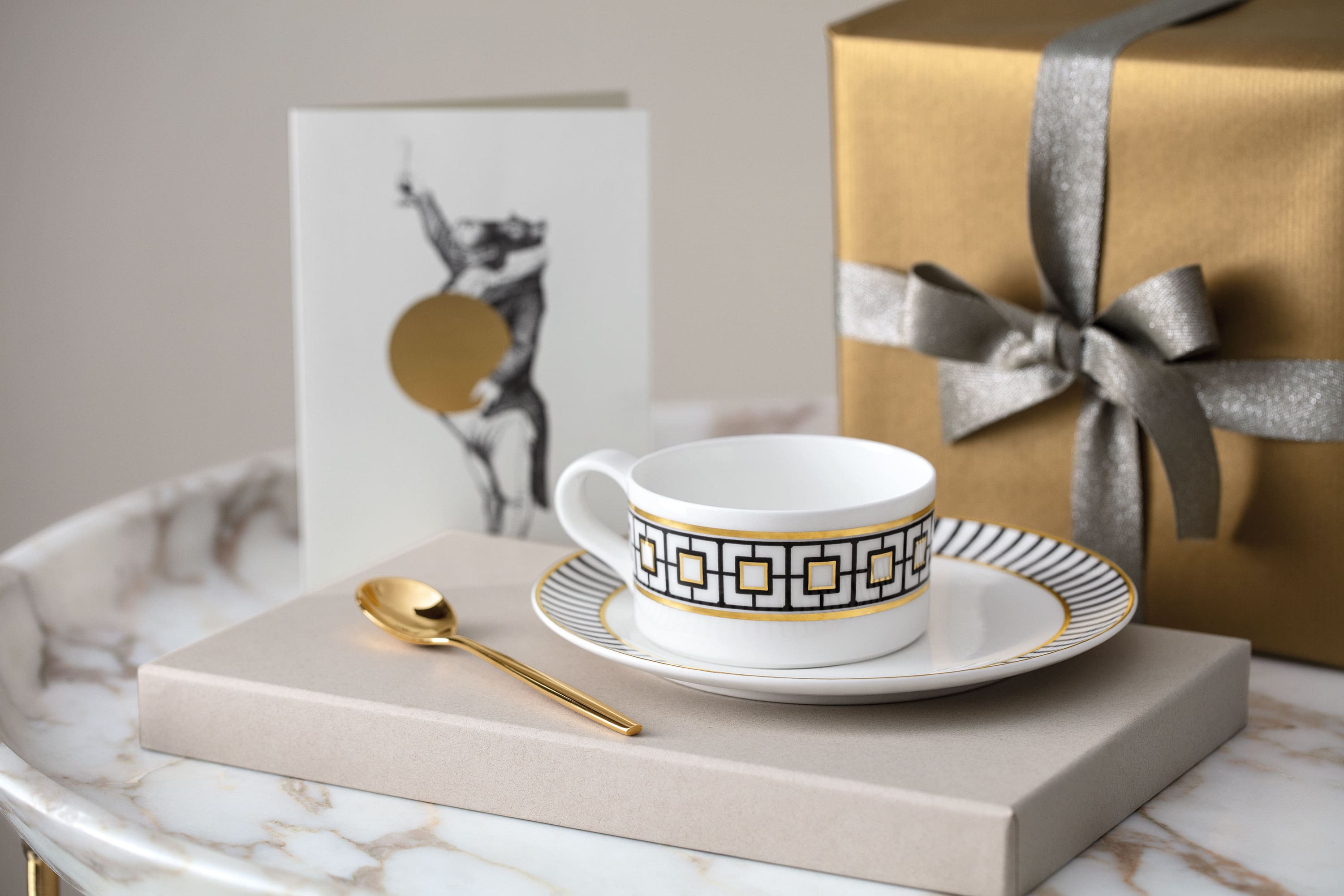 A golden MetroChic tea cup and saucer on a marble table.